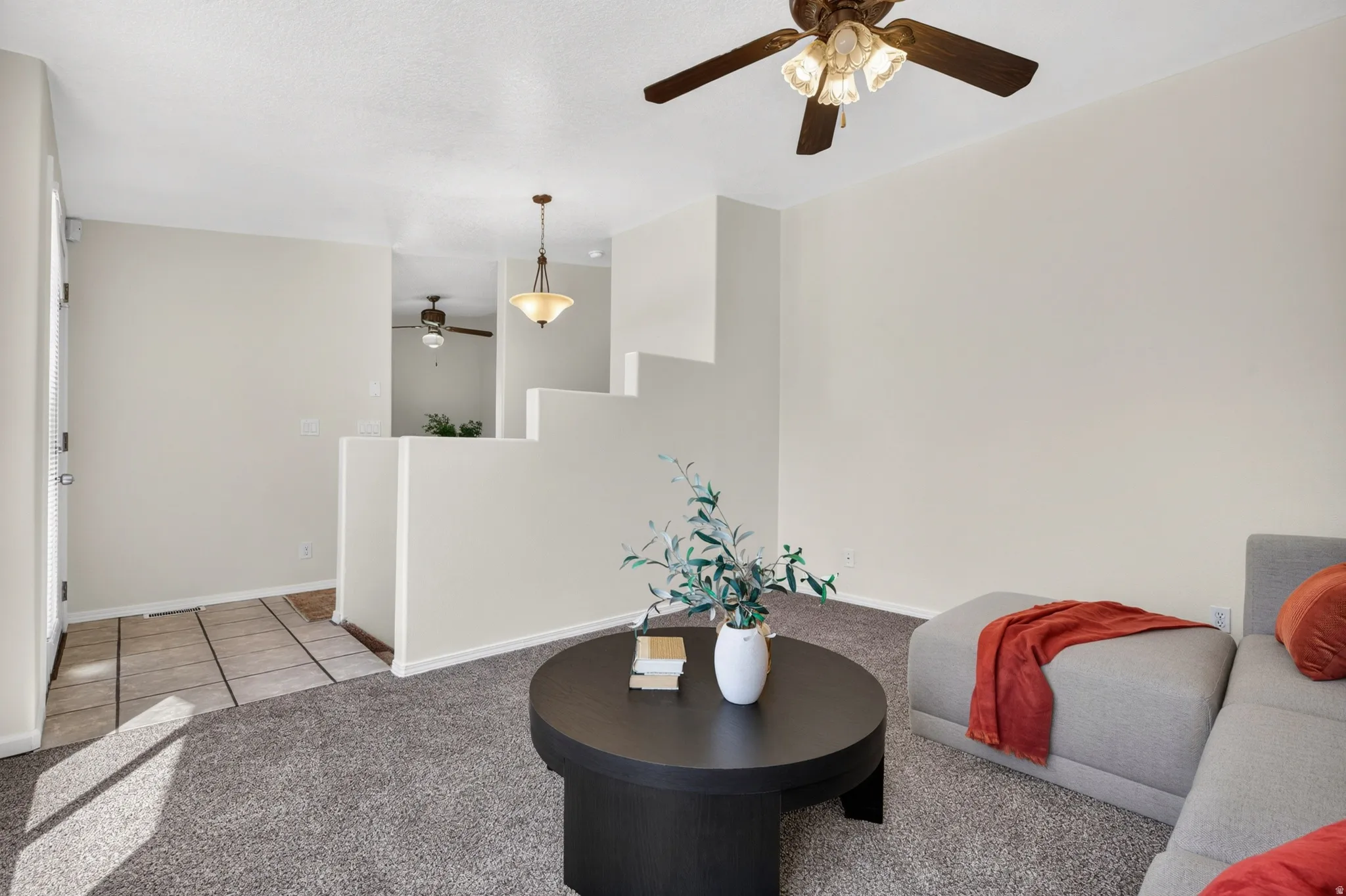Carpeted living area with a ceiling fan, neutral wall paint, and a tiled entry