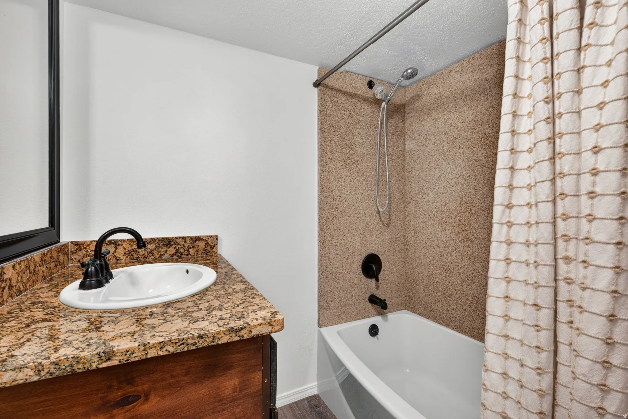 Tub and shower combination with a handheld shower head, a single basin sink, a rich wood-finish vanity, and a speckled countertop