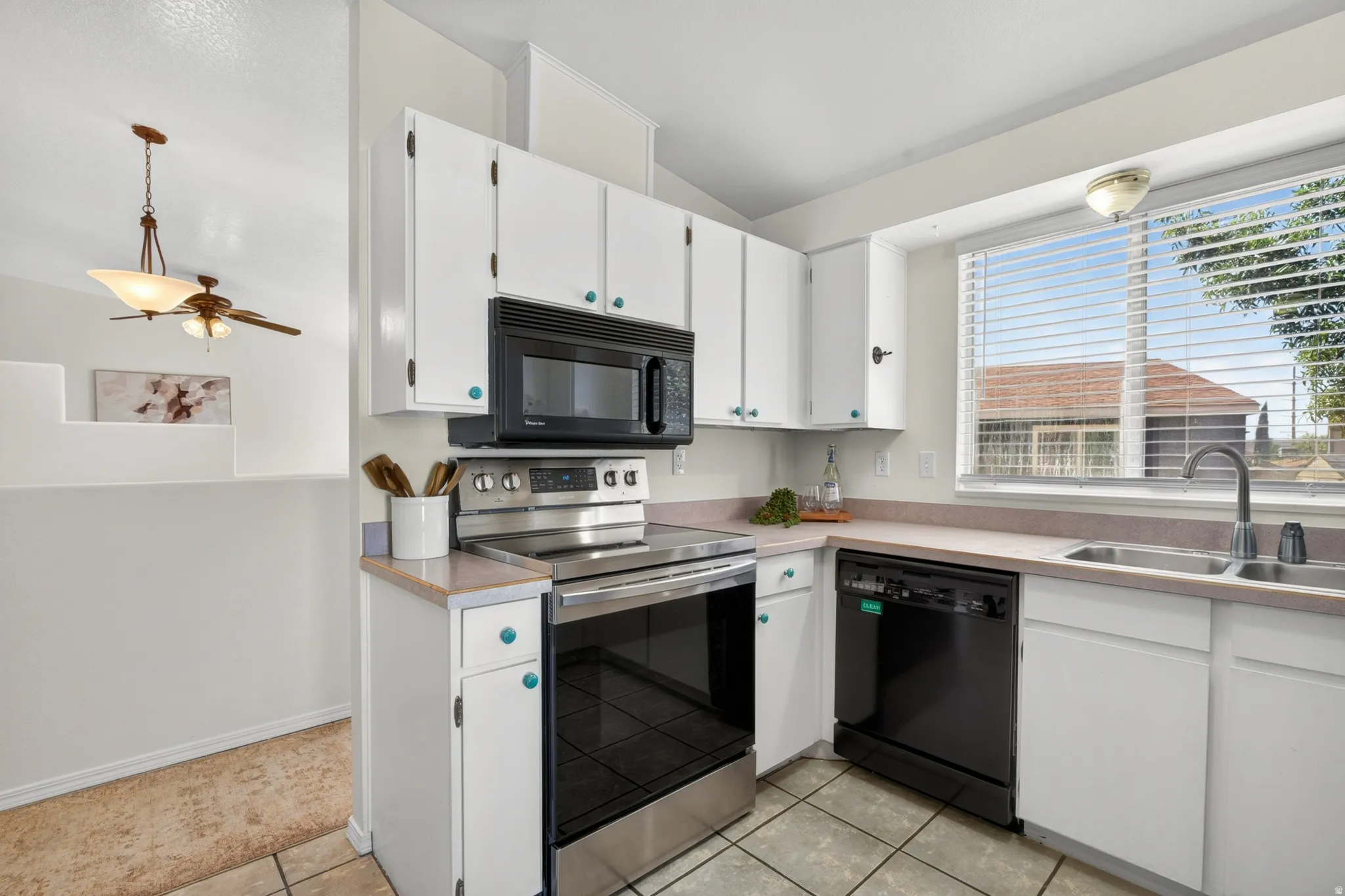 Kitchen featuring white cabinetry, an over-range microwave, stainless steel and black appliances, tile flooring, and a double basin sink