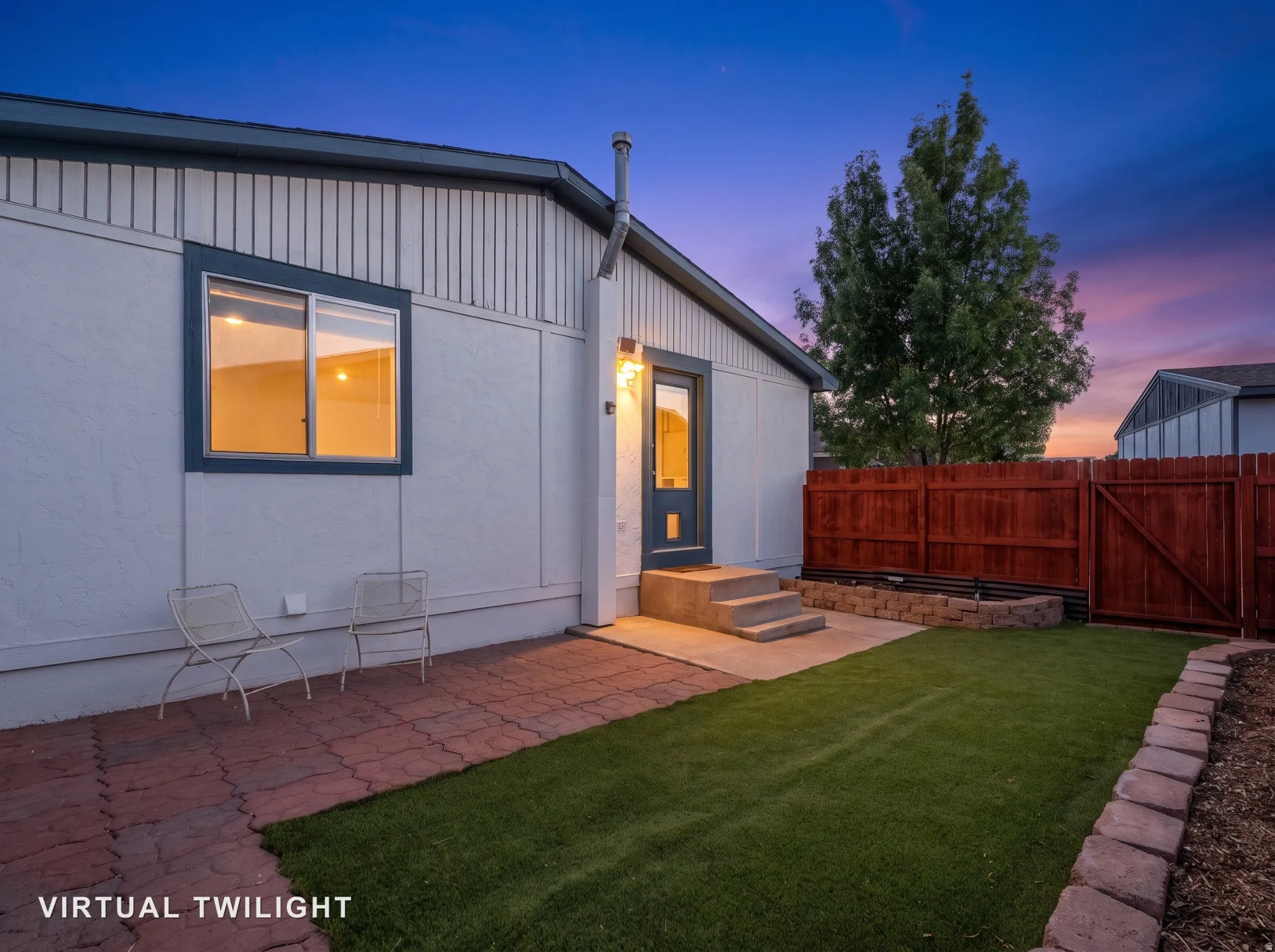 Expansive backyard featuring a manicured lawn, brick paver patio, wood privacy fence, and concrete steps to the entrance