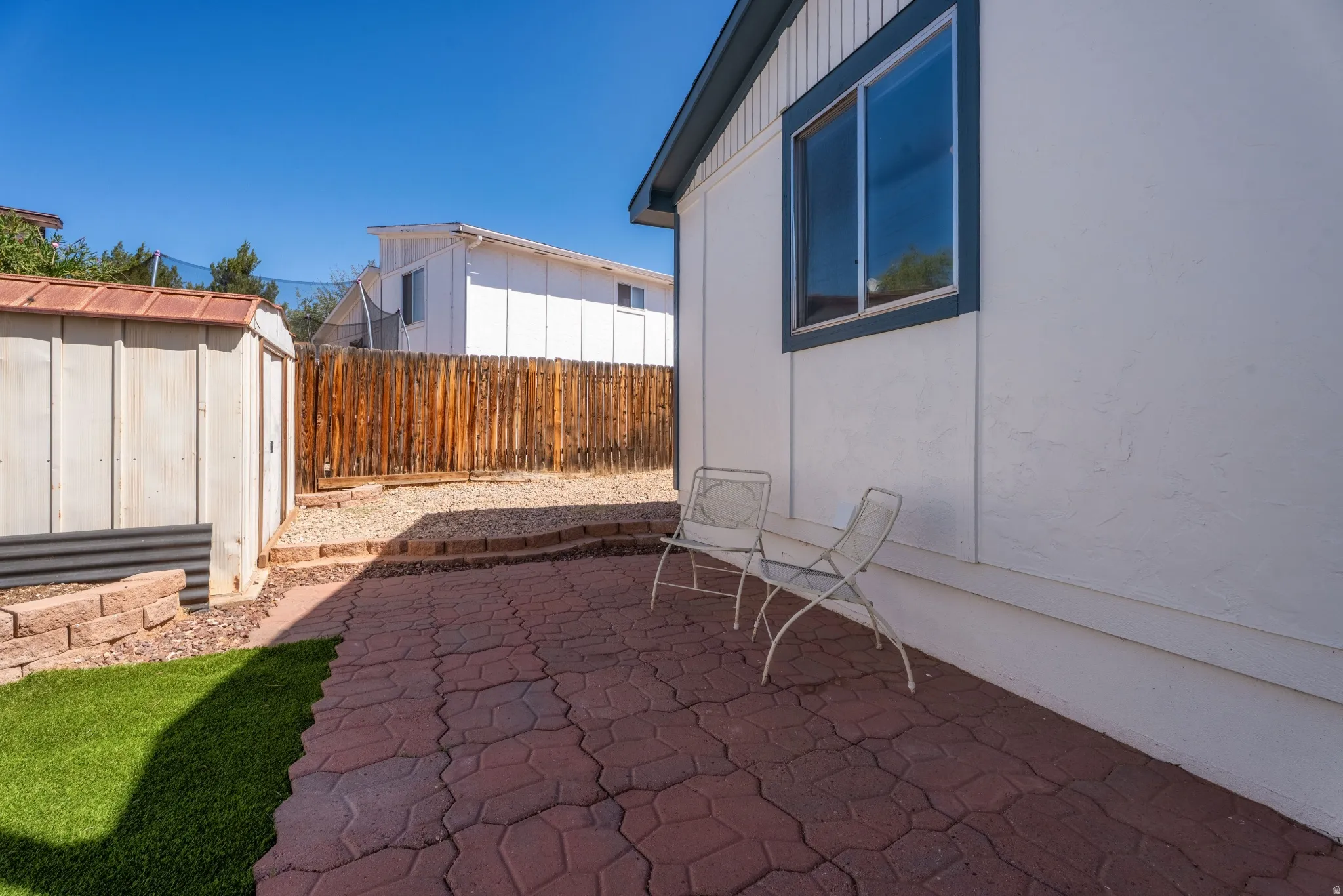 Textured paver patio with a low retaining wall, artificial turf section, privacy fencing, and an exterior storage shed