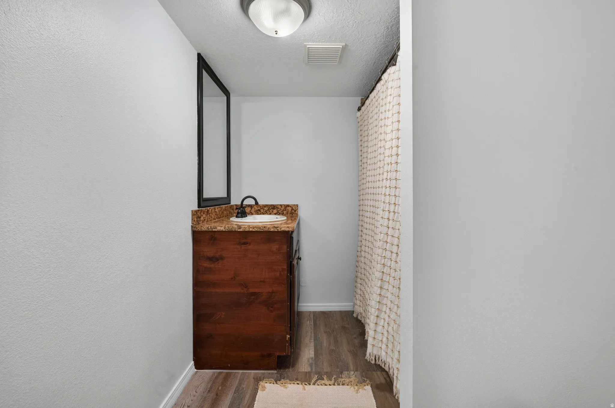 Wood-finish flooring, dark wood vanity cabinet, stone-finish countertop, framed mirror, and ceiling-mounted light fixture