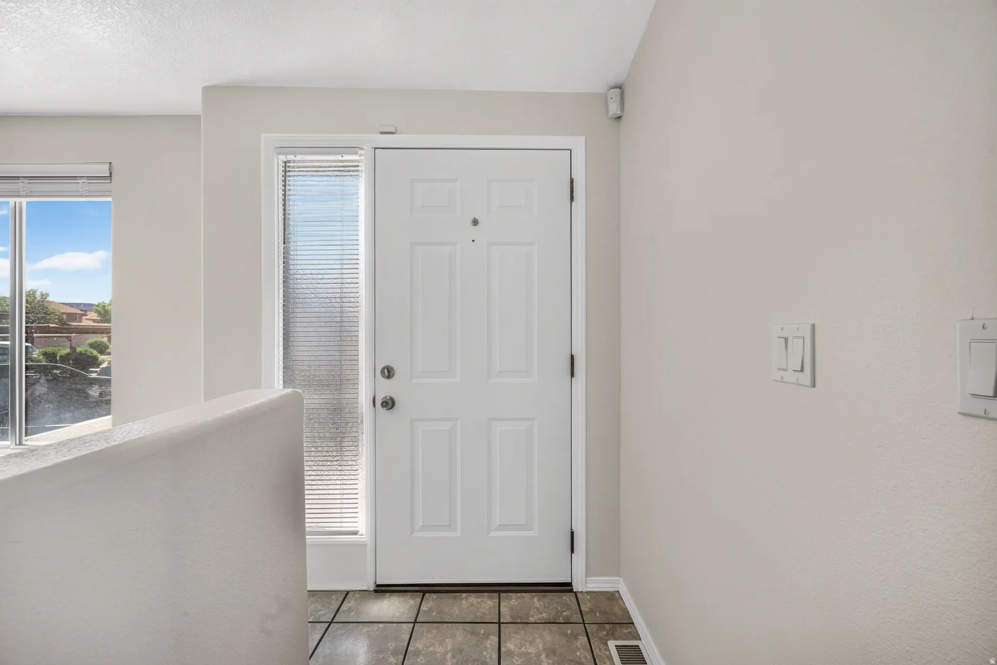 White paneled door with a sidelight, ceramic tile flooring, and a window with blinds