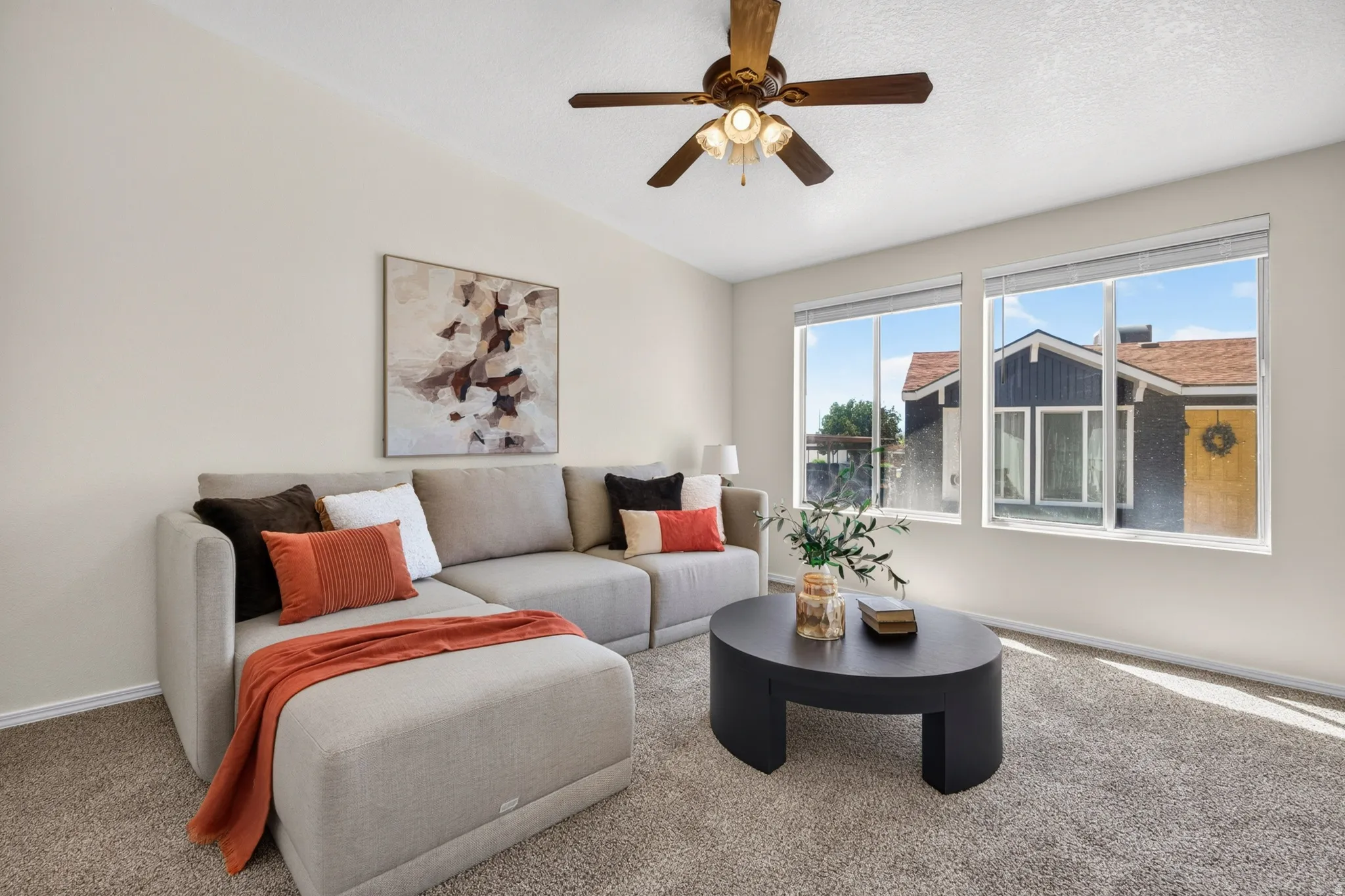 Carpeted living space featuring an angled ceiling, ceiling fan, and two large windows
