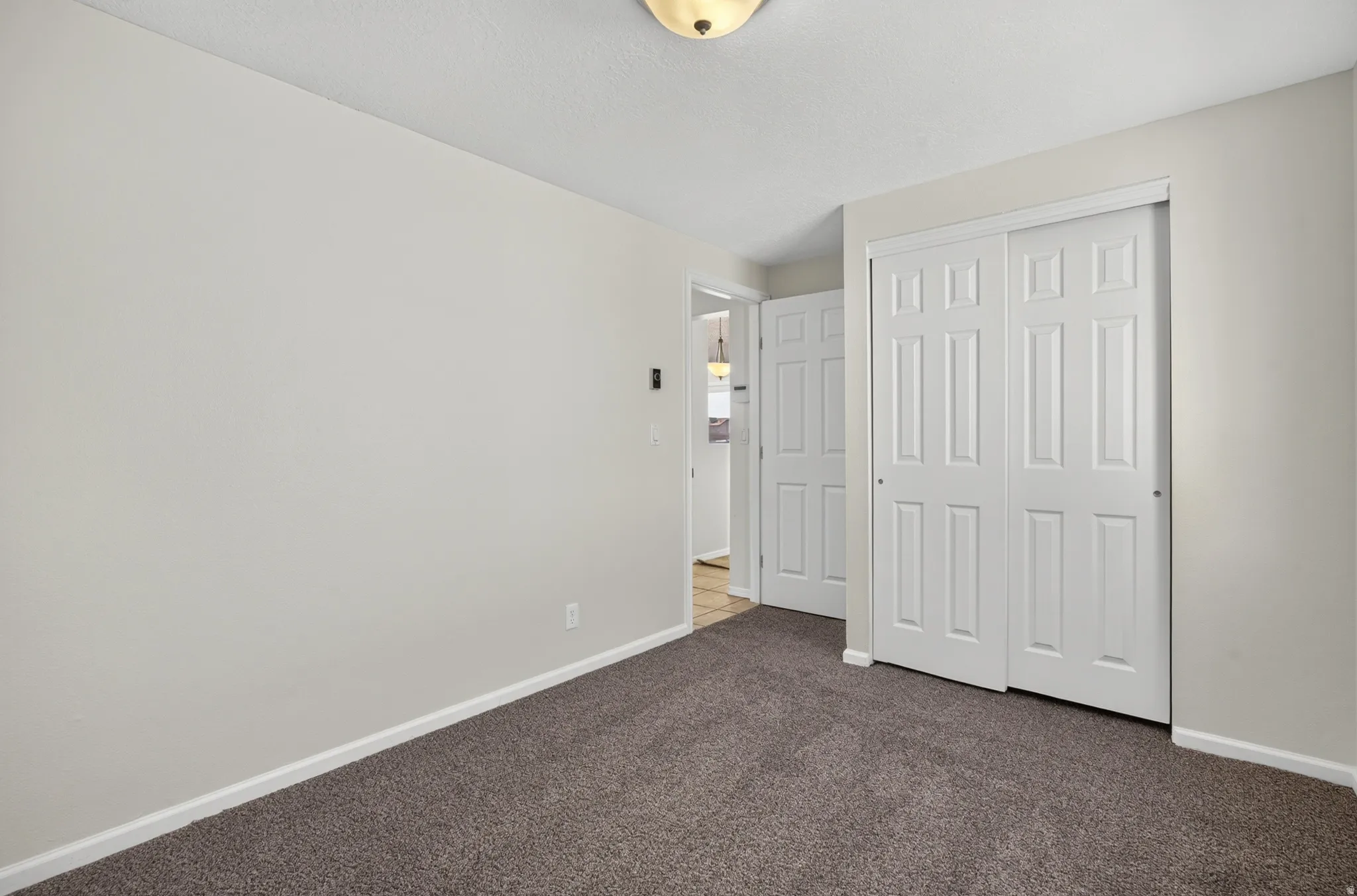 Plush carpet flooring, white painted walls, white trim, and white bi-fold closet doors