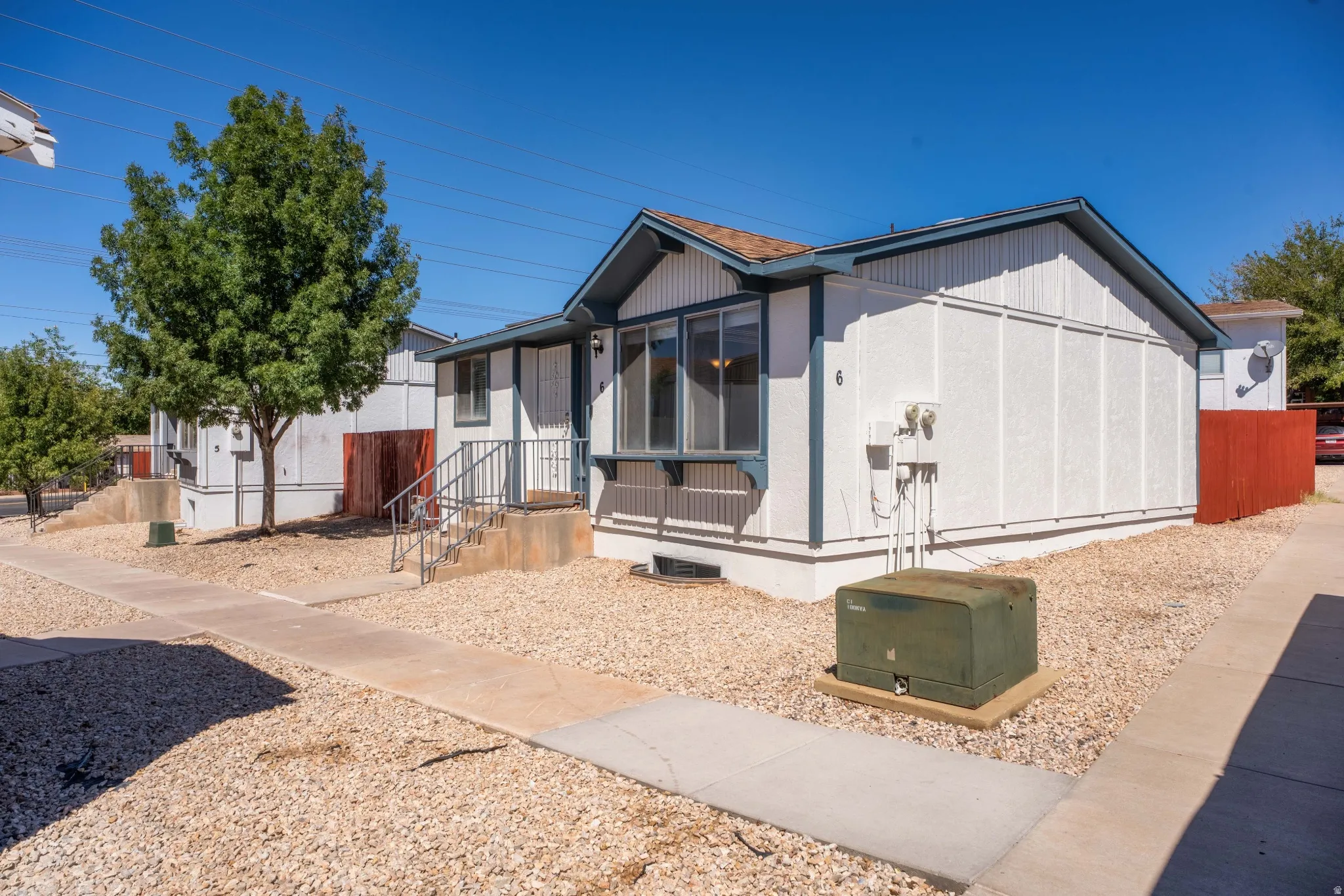 Exterior featuring a covered entry, concrete steps with metal railings, and a gravel-covered yard