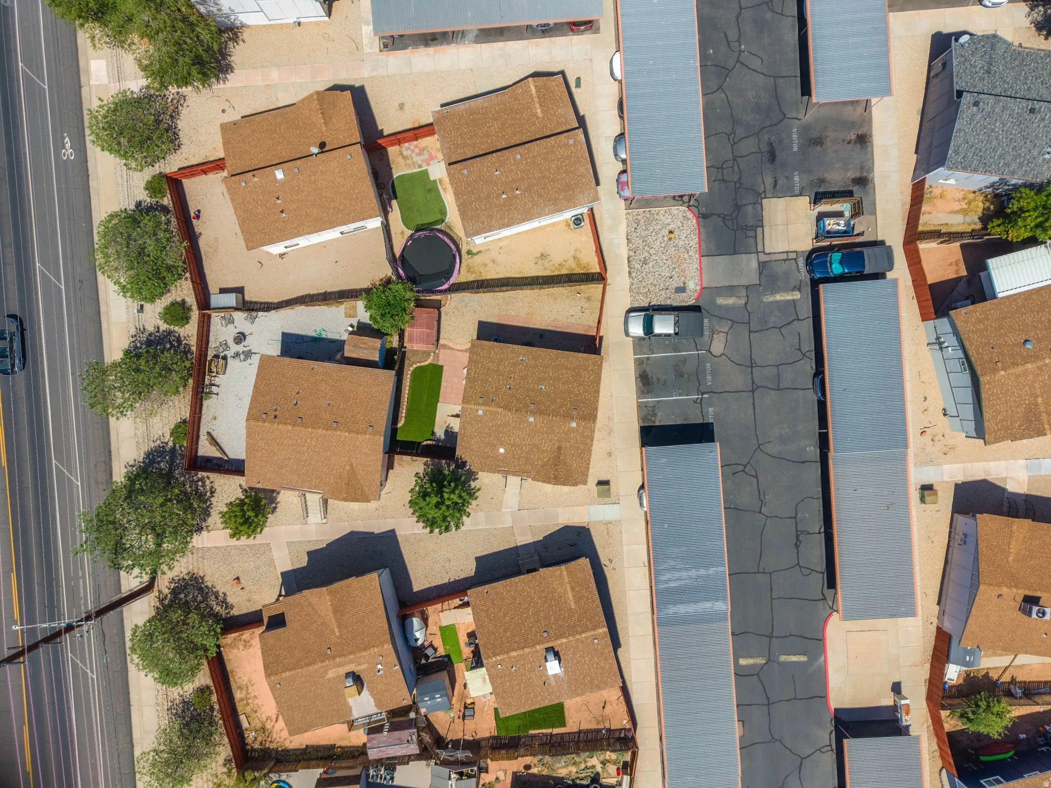 Multiple residential structures with individual fenced yards, paved parking areas, and mature trees