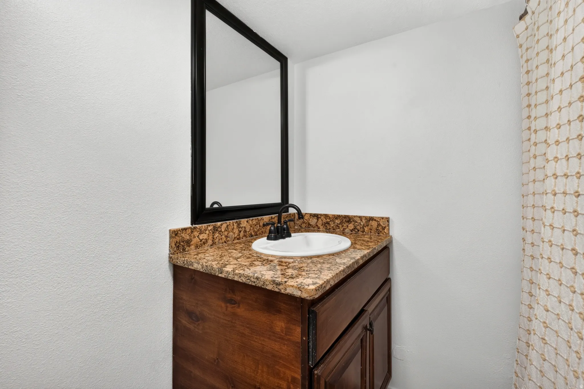 Vanity with a granite countertop, undermount sink, dark wood-finish cabinetry, and a framed mirror