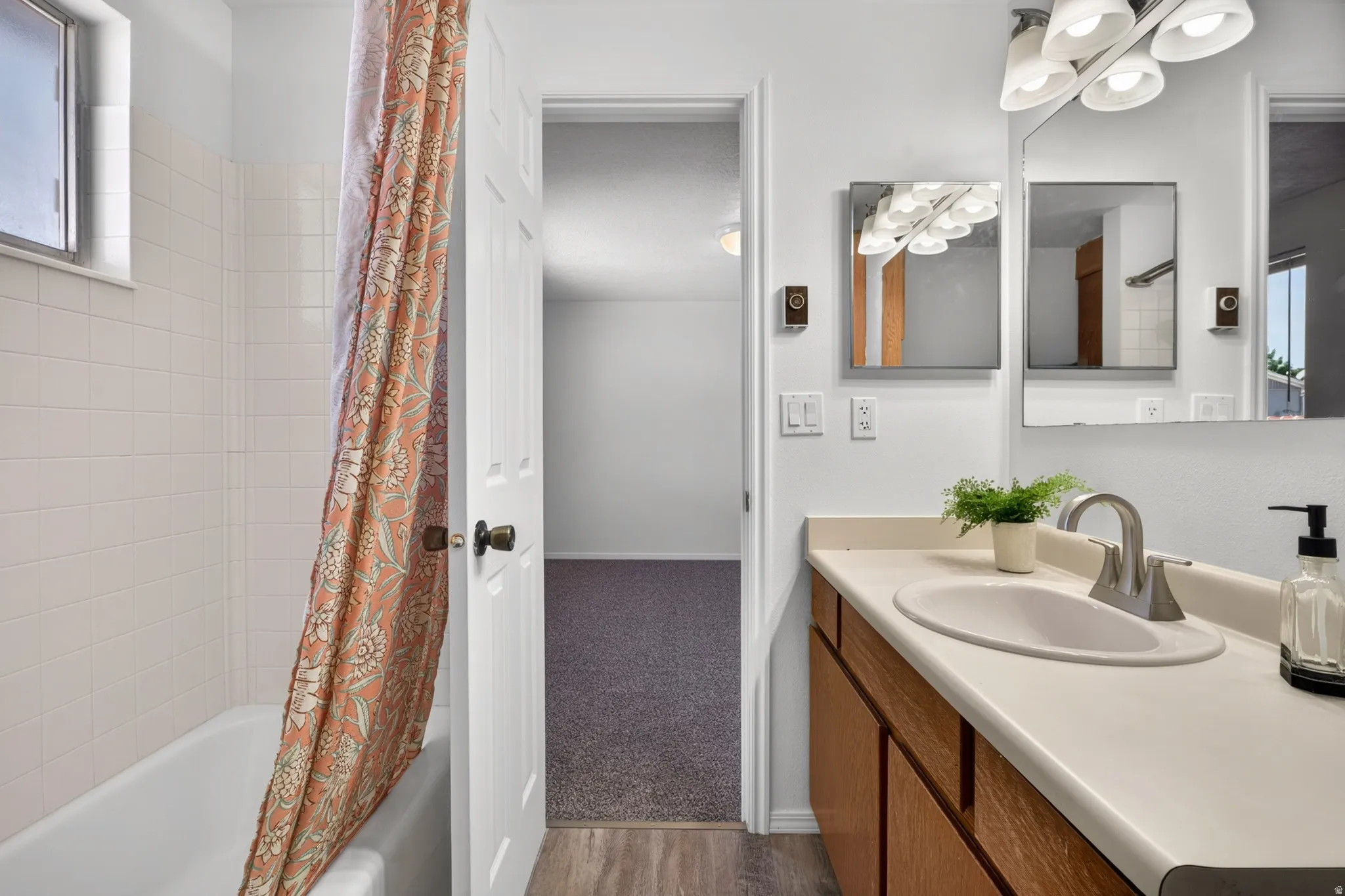 Bathroom featuring a white bathtub, white tiled shower surround, light-toned vanity with an integrated sink, brushed nickel faucet, and a multi-bulb vanity light fixture