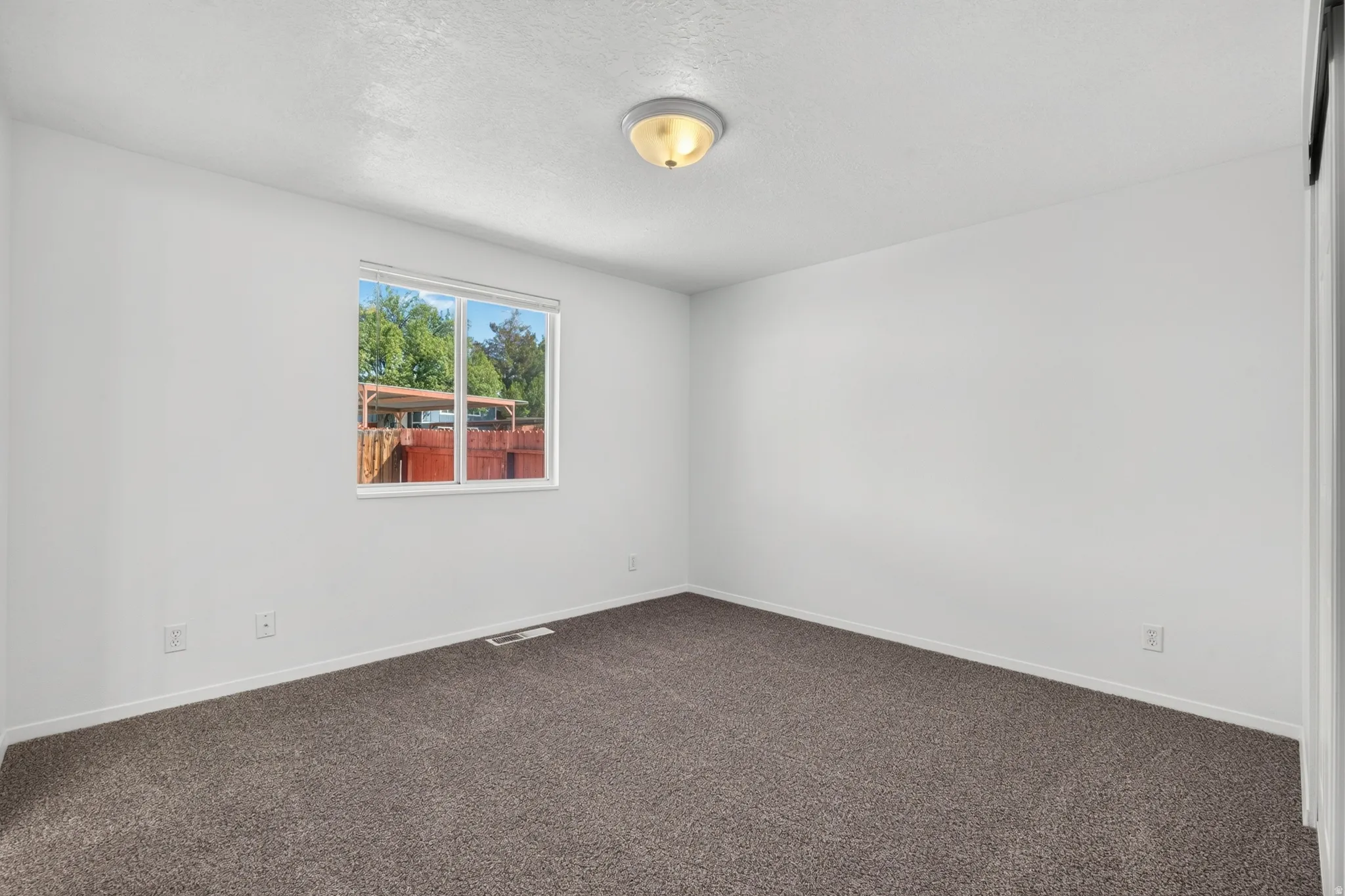 Neutral wall paint, textured ceiling, flush mount ceiling light, and window with exterior landscaping