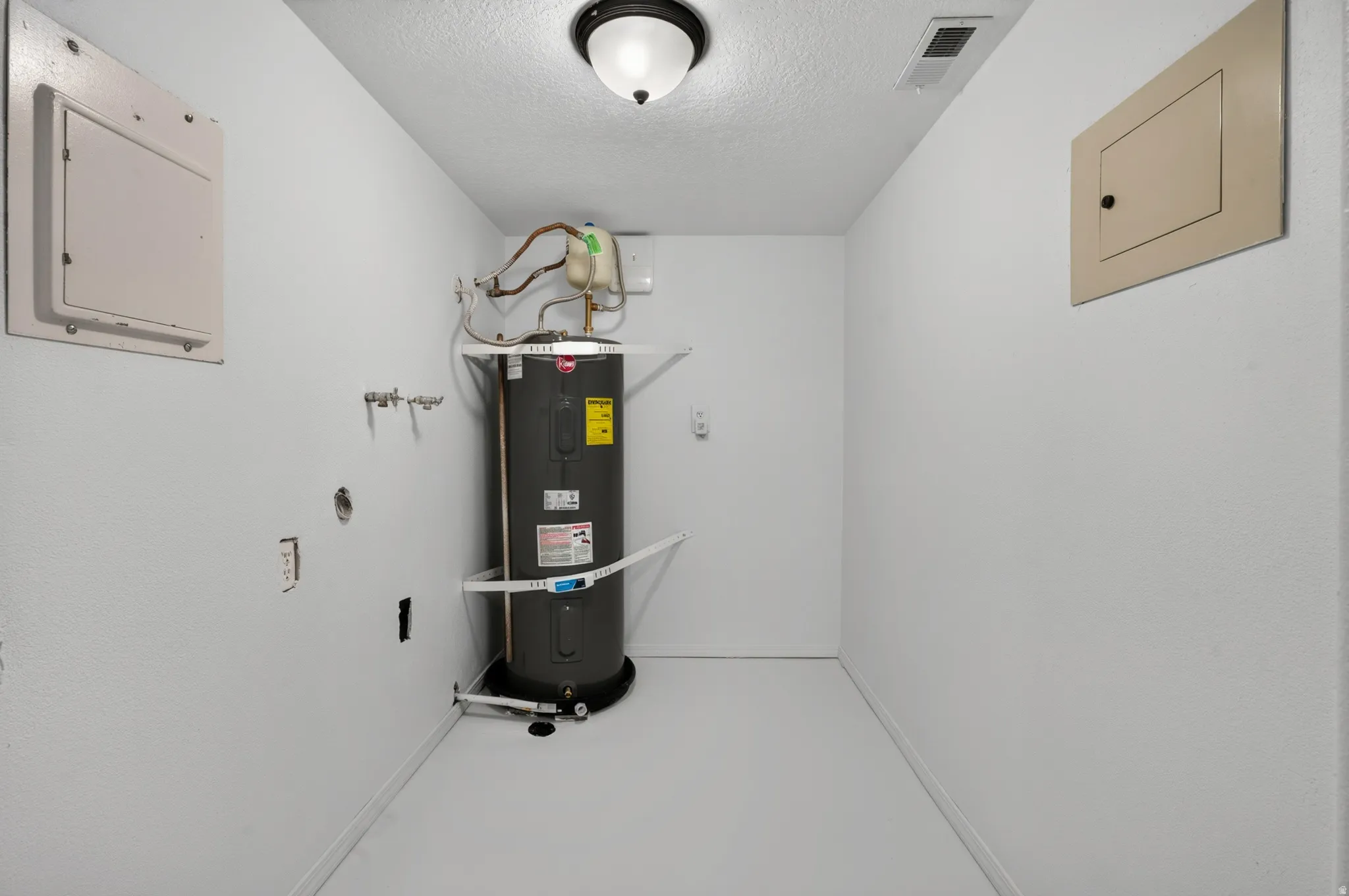 Utility room with water heater installation, wall-mounted access panels, and overhead lighting