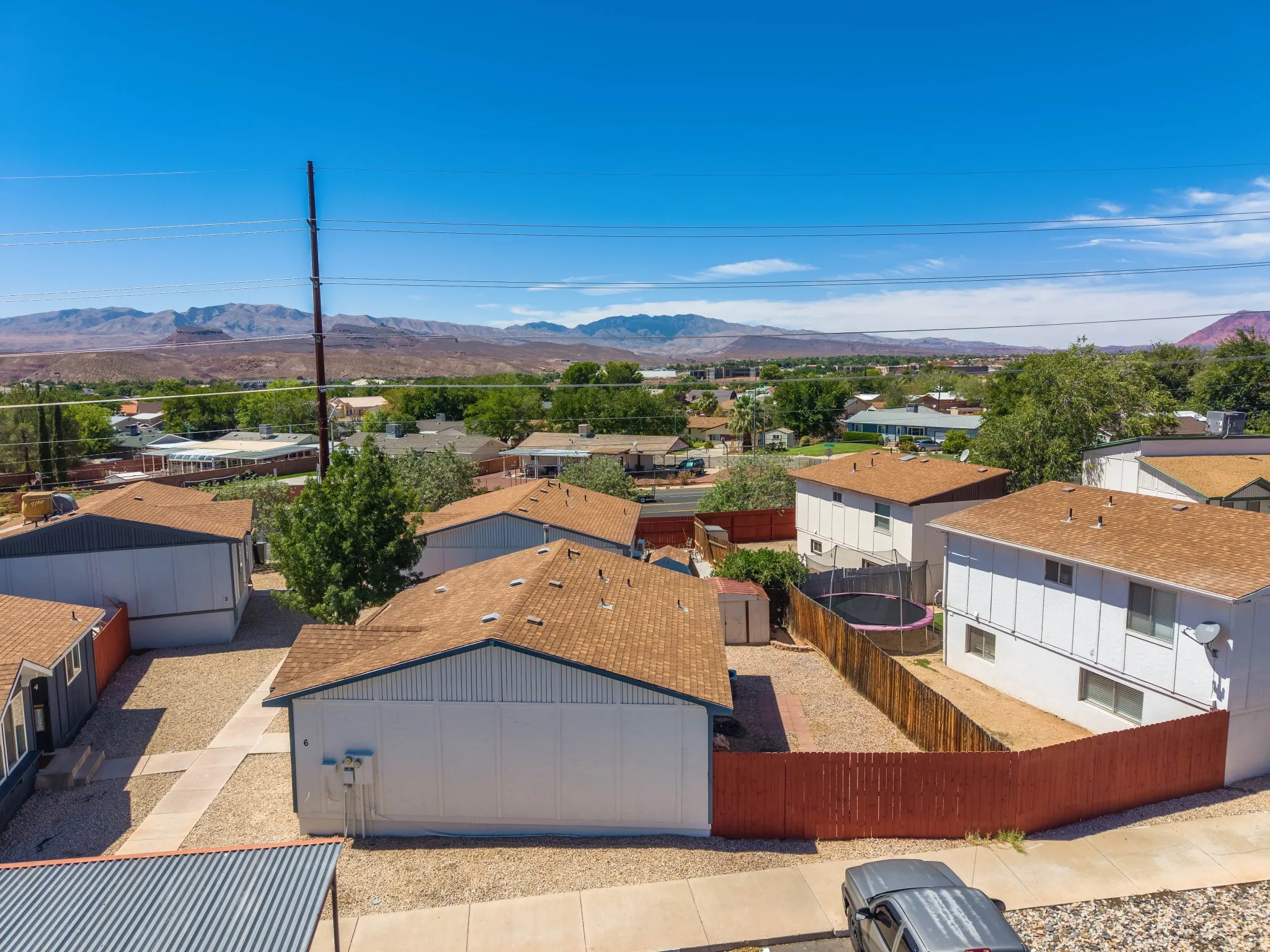 Expansive mountain scenery, multiple properties with shingle roofs, gravel landscaping, and a red wood fence