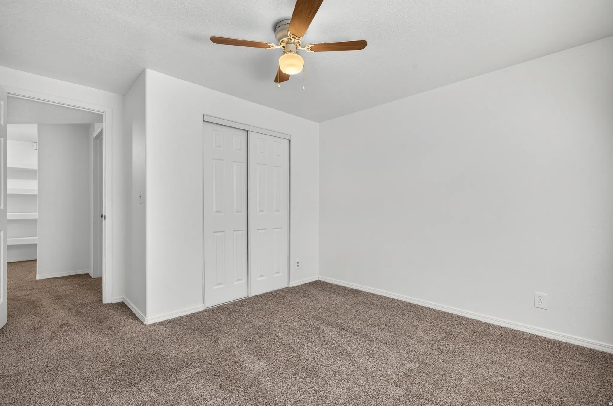 Neutral wall finish, carpeted flooring, ceiling fan with light fixture, sliding closet doors, and hallway access