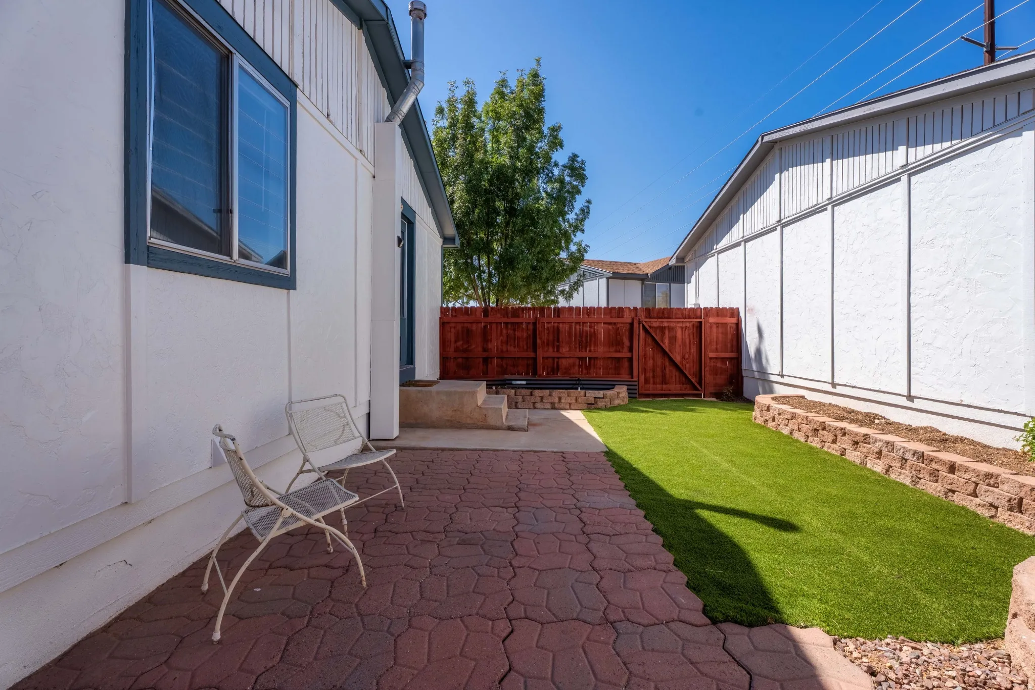Paved patio with decorative pavers, artificial turf lawn, and raised garden beds with stone retaining walls