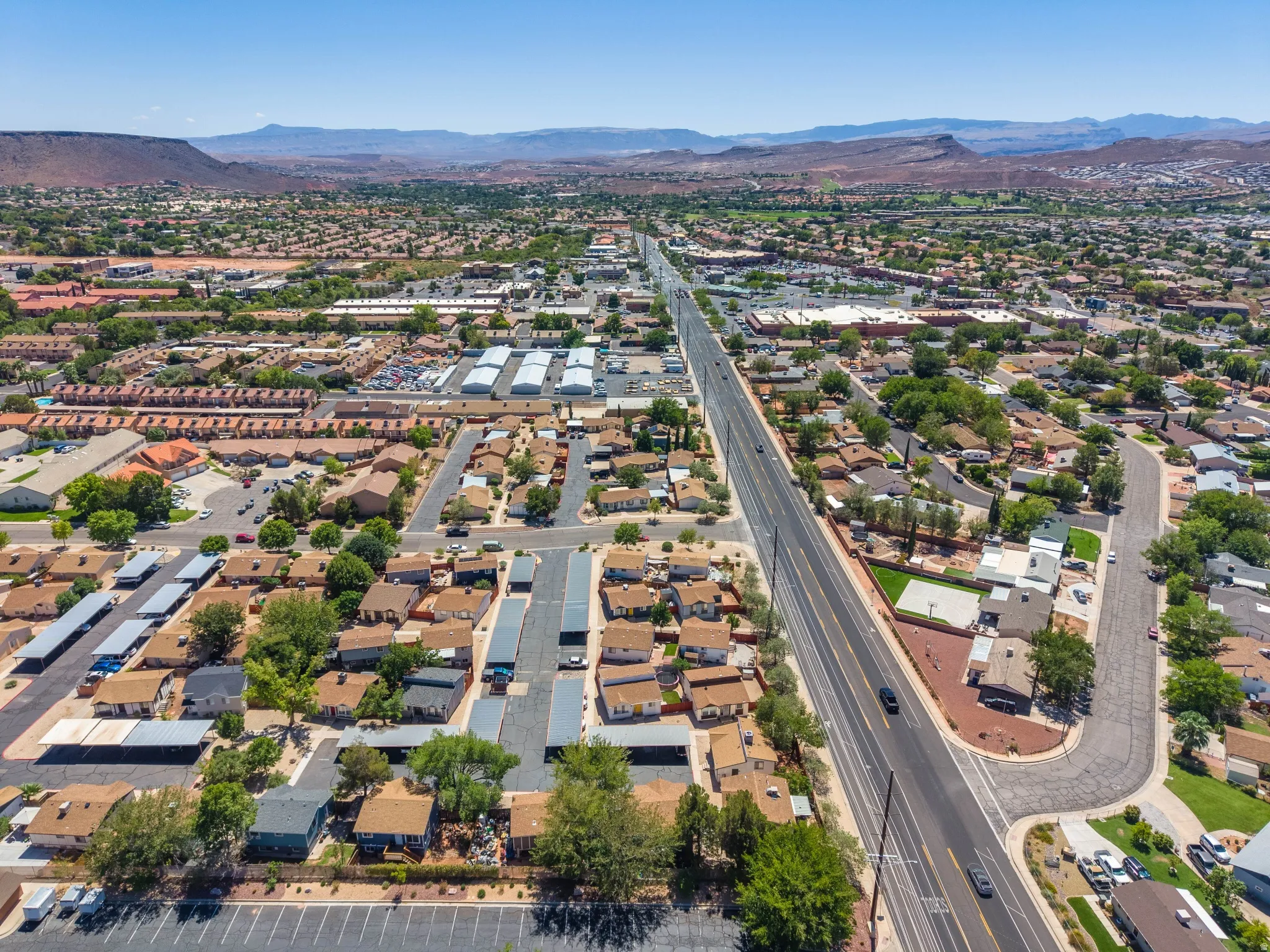 Expansive community with a prominent paved road, diverse residential structures, and distant mountainous terrain