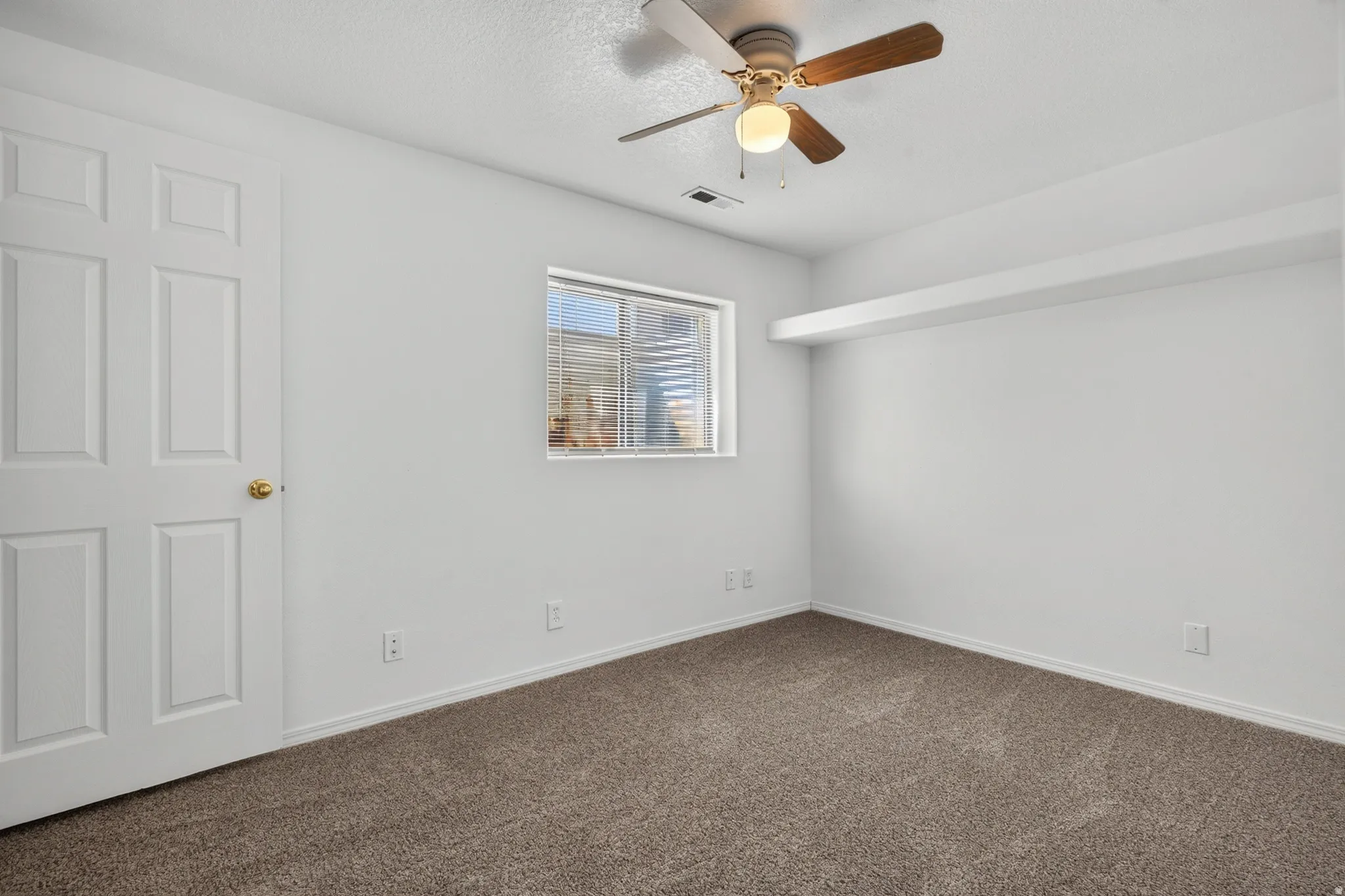 Neutral wall color, window with blinds, overhead ceiling fan with light fixture, paneled door, and carpeted flooring