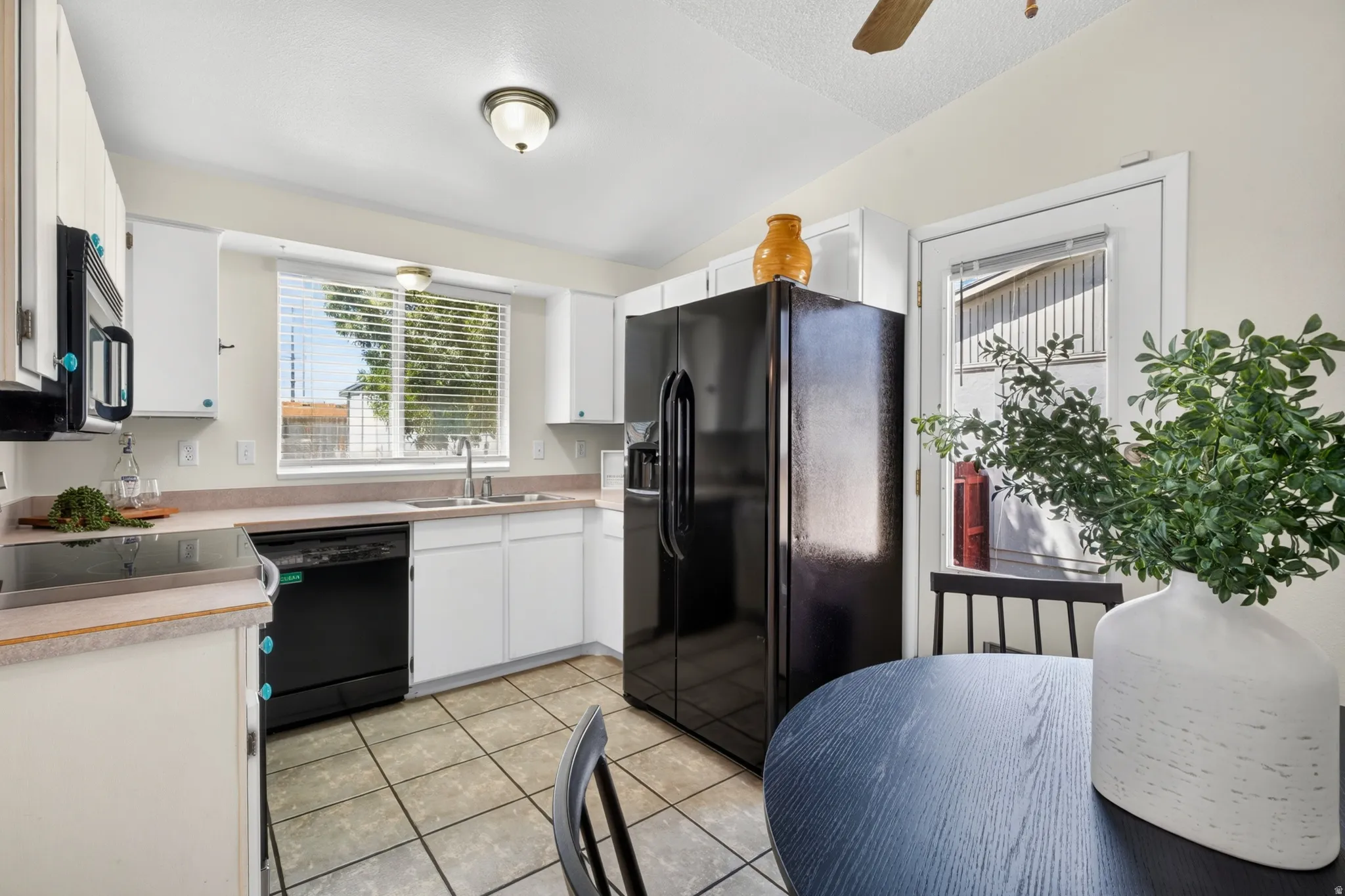 Kitchen featuring white cabinetry, black appliances, tile flooring, a window above the sink, and a glass-paned exterior door