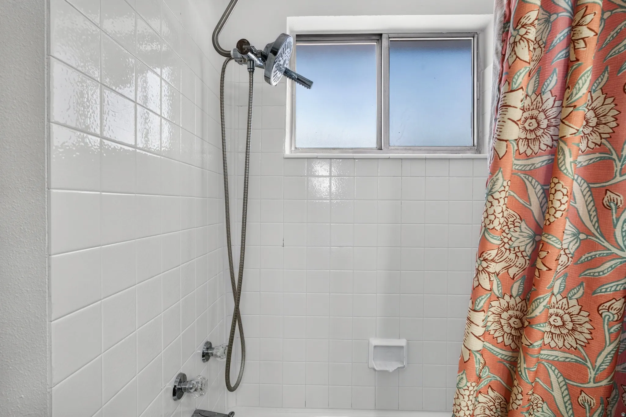 White tiled shower surround with a window, handheld showerhead, and bathtub faucet