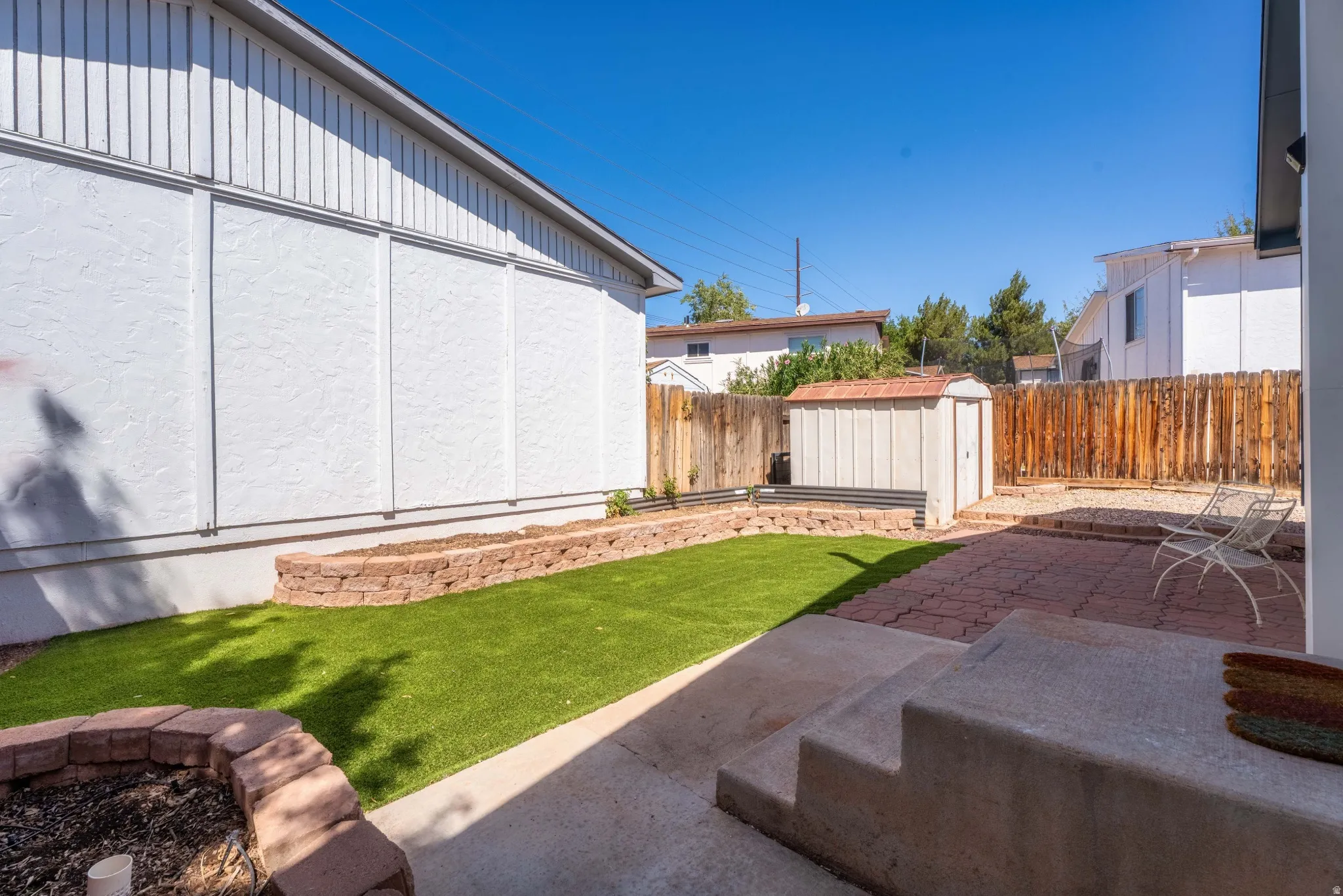 Backyard featuring artificial turf, a paver patio, a storage shed, and a privacy fence