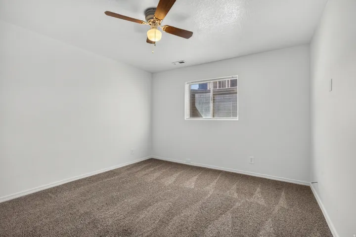 Neutral wall paint, window with blinds, ceiling fan with integrated lighting, and carpet flooring