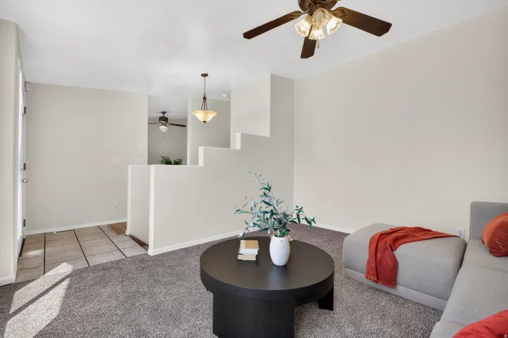 Carpeted living area with a ceiling fan, neutral wall paint, and a tiled entry