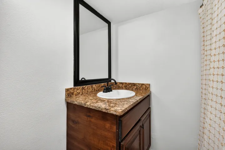 Vanity with a granite countertop, undermount sink, dark wood-finish cabinetry, and a framed mirror