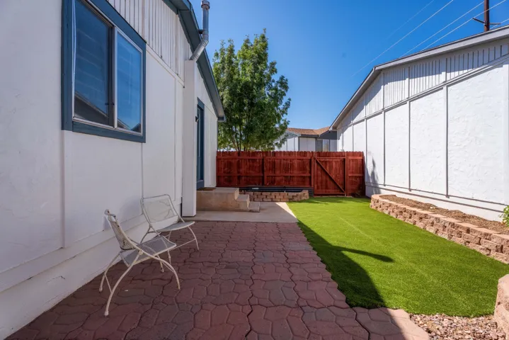 Paved patio with decorative pavers, artificial turf lawn, and raised garden beds with stone retaining walls
