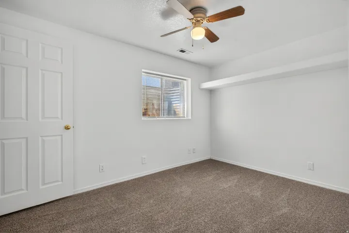 Neutral wall color, window with blinds, overhead ceiling fan with light fixture, paneled door, and carpeted flooring