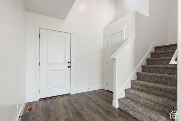 Wood-finish flooring, white paneled doors with black hardware, and carpeted stairs with white railing