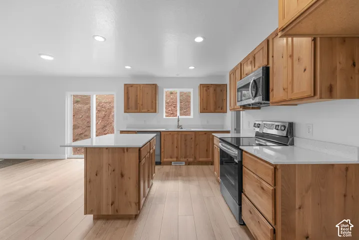 Kitchen featuring natural wood-finish cabinetry, light-toned countertops, a central island, and stainless steel appliances