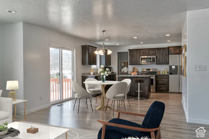 Wood-finish flooring throughout, sliding glass door with balcony access, recessed ceiling lighting, kitchen with dark wood cabinetry, and stainless steel appliances