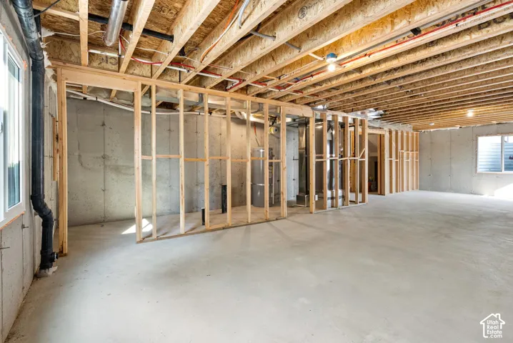 Unfinished basement with concrete flooring, exposed wood framing, concrete foundation walls, and multiple windows