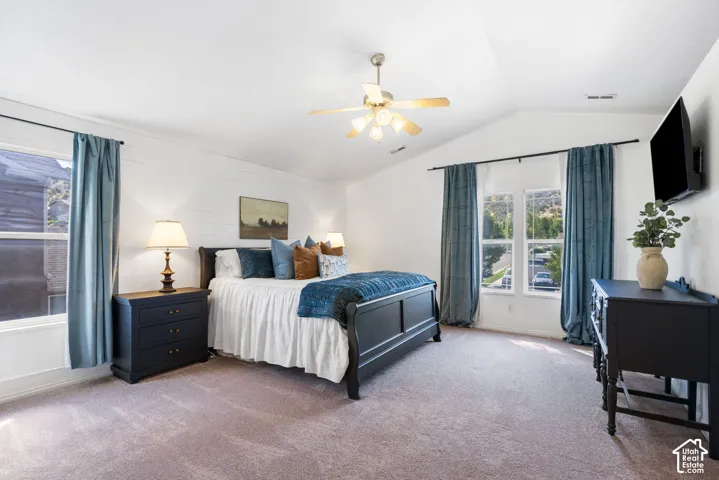 Vaulted ceiling with a ceiling fan, shiplap accent wall, two large windows, and carpet flooring