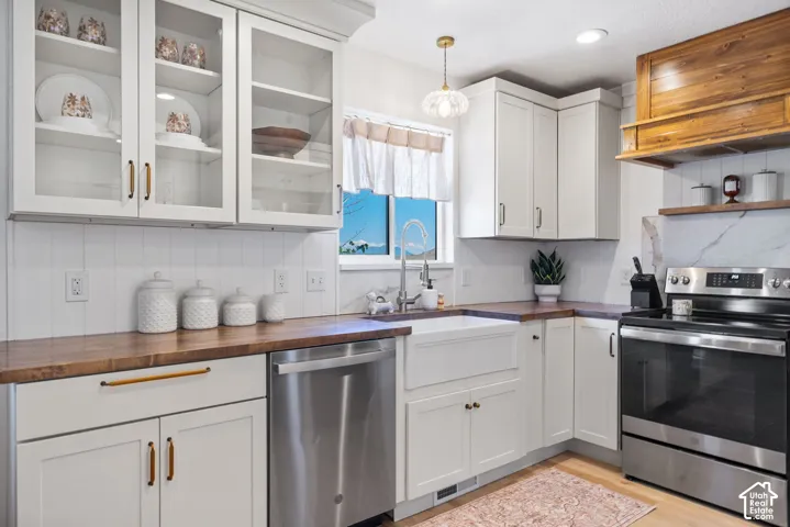 White shaker cabinetry with glass-front uppers, wood-finish countertops, stainless steel appliances, and a farmhouse-style sink