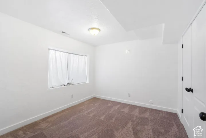 Window with white curtains, neutral wall paint, ceiling-mounted light fixture, and warm-toned patterned carpeting