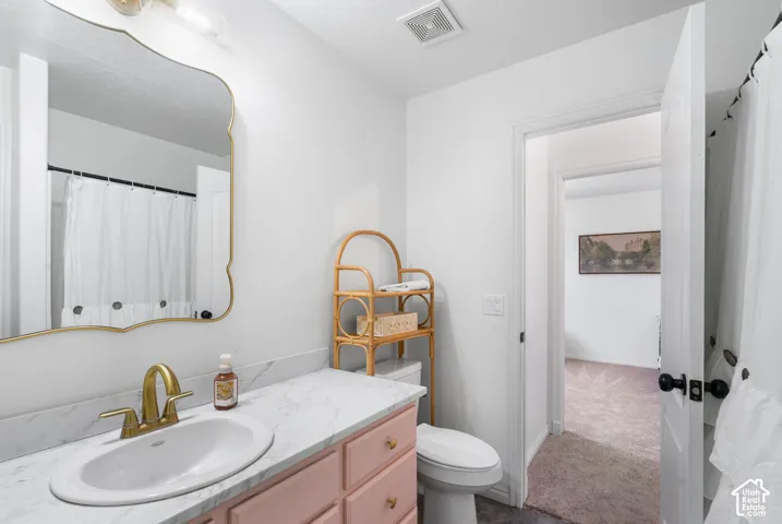 White vanity with a single basin sink, brass-finish faucet, and light-toned countertop
