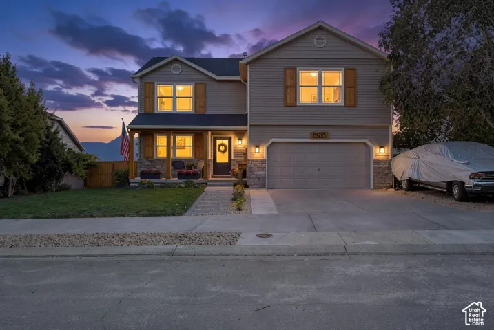 Siding exterior with stone accents, a covered front porch, an attached two-car garage, and a concrete driveway