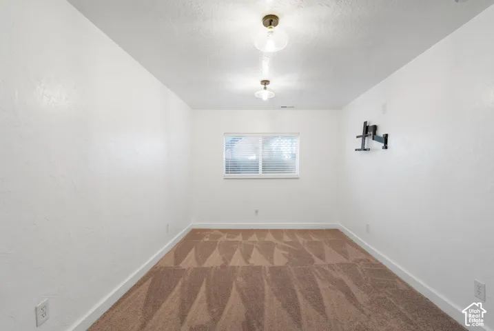 Recessed window with horizontal blinds, two ceiling-mounted light fixtures, textured walls, and patterned carpet flooring