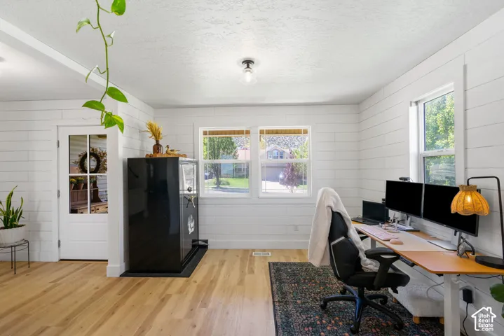 Light wood-finish flooring, white shiplap walls, multiple windows, recessed ceiling lighting, and a glass-paneled door