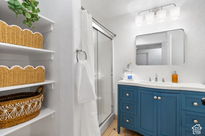 Bathroom with a blue vanity, a rectangular mirror, a four-light fixture, built-in open shelving, and a glass-enclosed shower