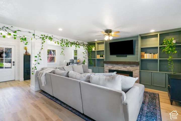 Built-in shelving, fireplace, ceiling fan, recessed lighting, and wood-finish flooring