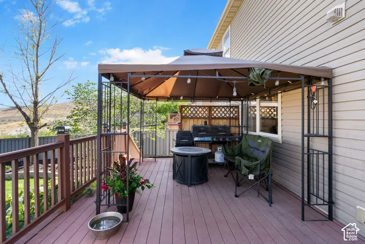 Expansive outdoor deck featuring wood-finish flooring, a wood railing, and a metal gazebo with string lighting