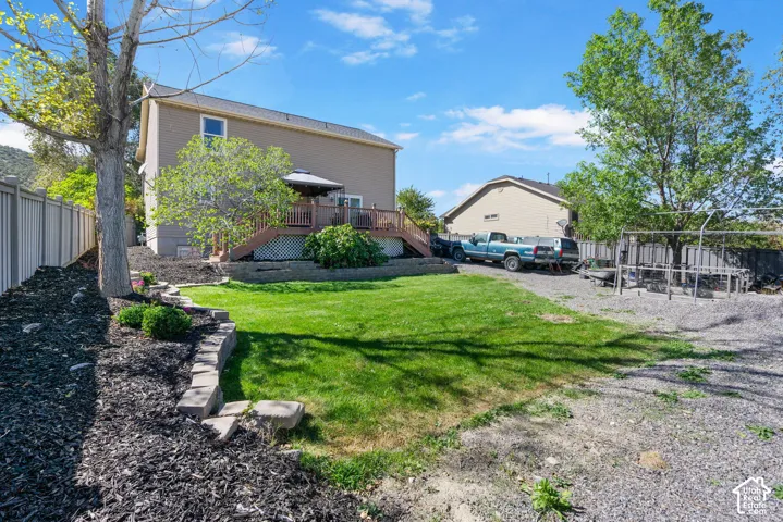 Expansive backyard featuring a manicured lawn, a gravel area, a multi-level deck, and a privacy fence
