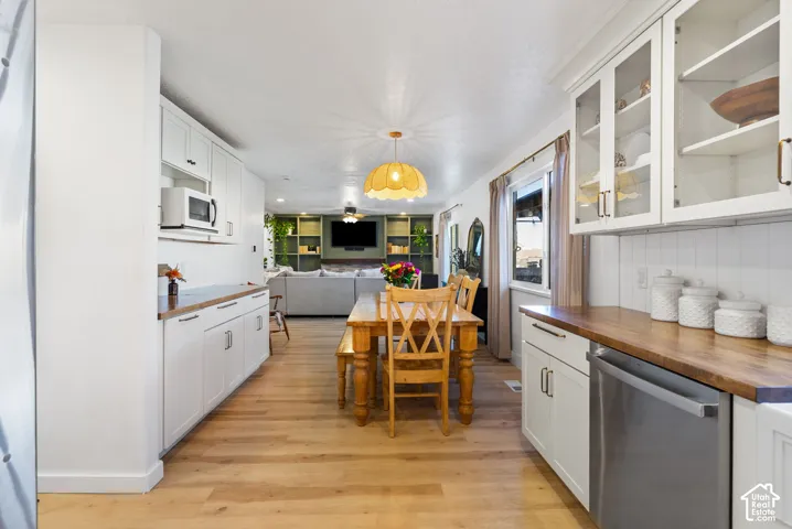 White shaker-style cabinetry with black hardware, wood-finish countertops, stainless steel appliances, and light wood-finish flooring