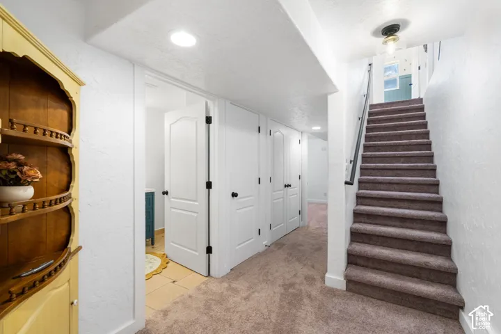 Carpeted staircase with dark handrail, recessed lighting, and white panel doors