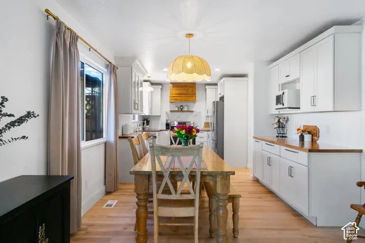 Open concept dining area with light wood-finish flooring, featuring a unique scalloped pendant light fixture, white perimeter cabinetry, and wood countertops