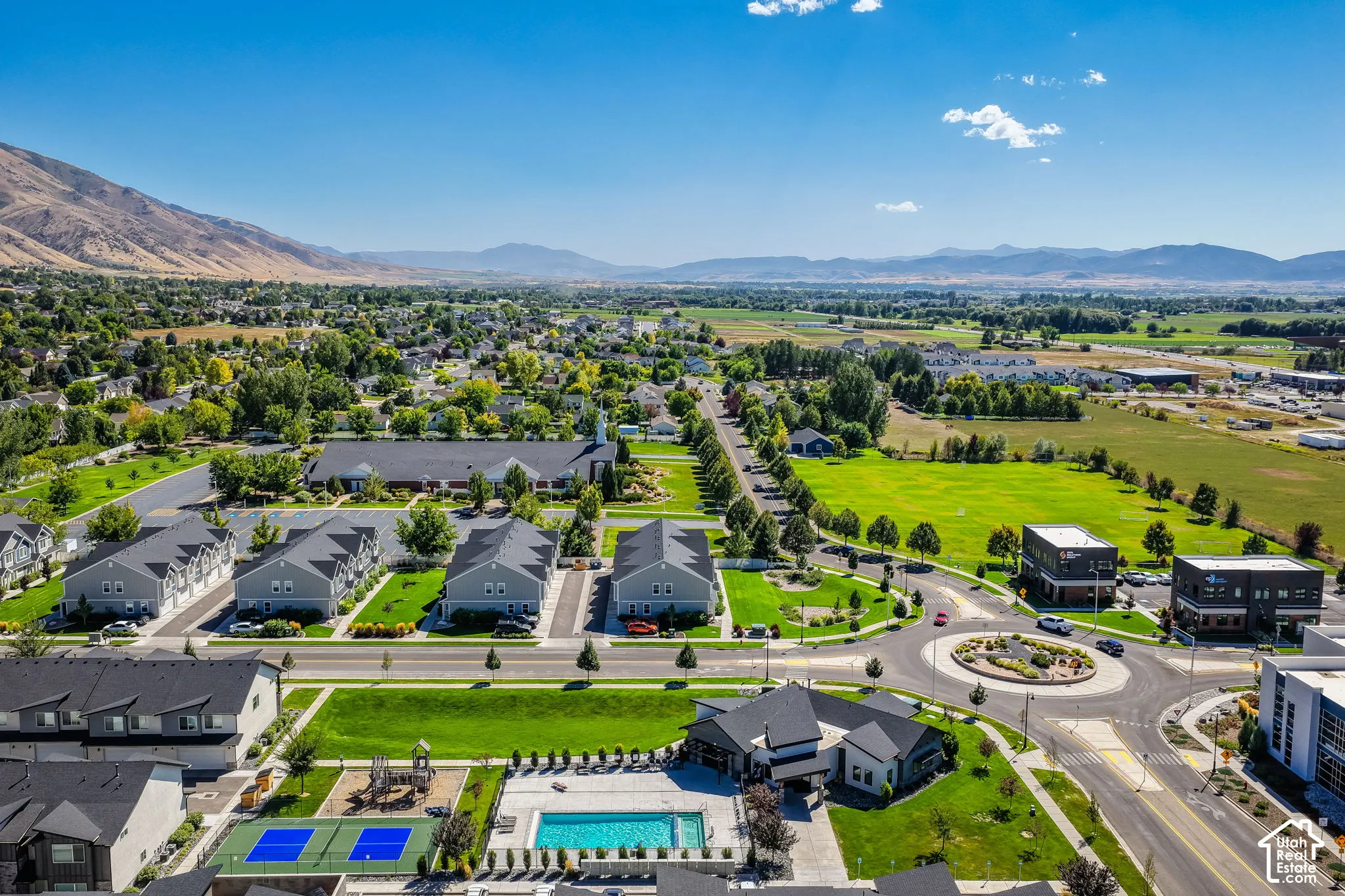 Community with mountain backdrop, featuring a swimming pool, sports courts, and a children's play area, surrounded by green spaces