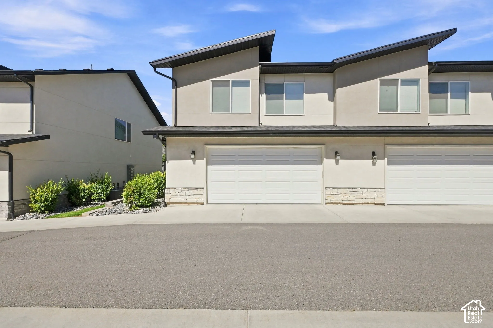 Contemporary exterior with stucco siding, white garage doors, and a stone accent facade