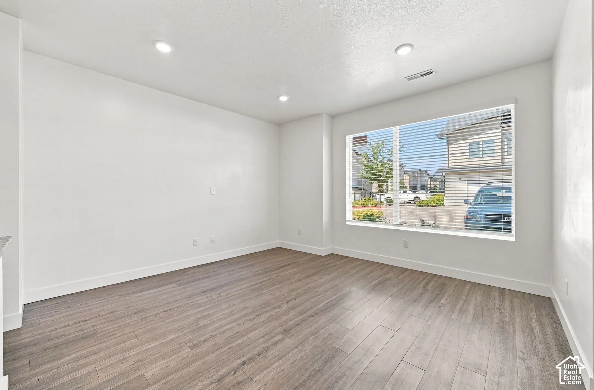 Recessed lighting, wood-finish flooring, white walls, large window with blinds, and white trim throughout