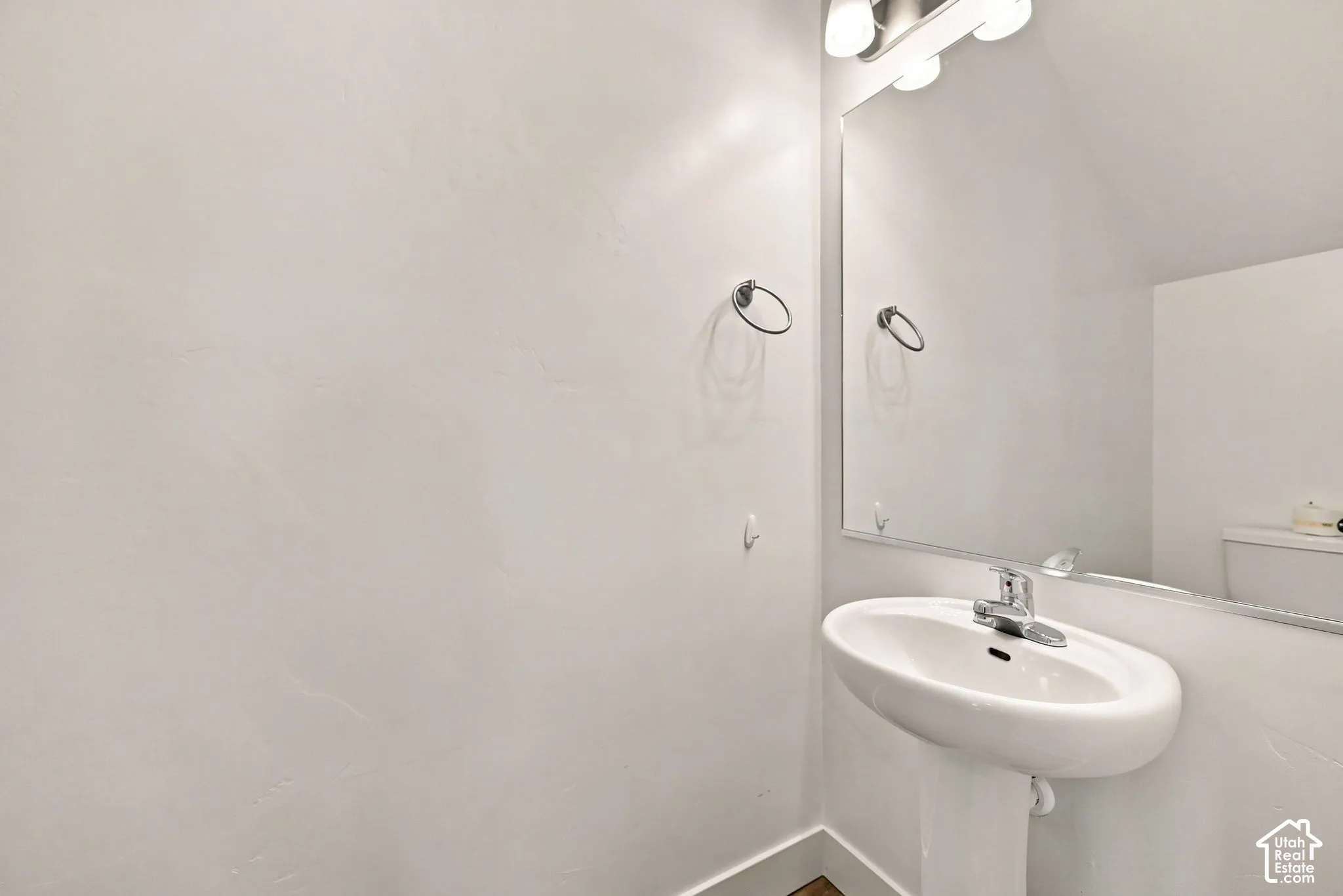 Pedestal sink with chrome faucet, wall-mounted mirror, and vanity light fixture